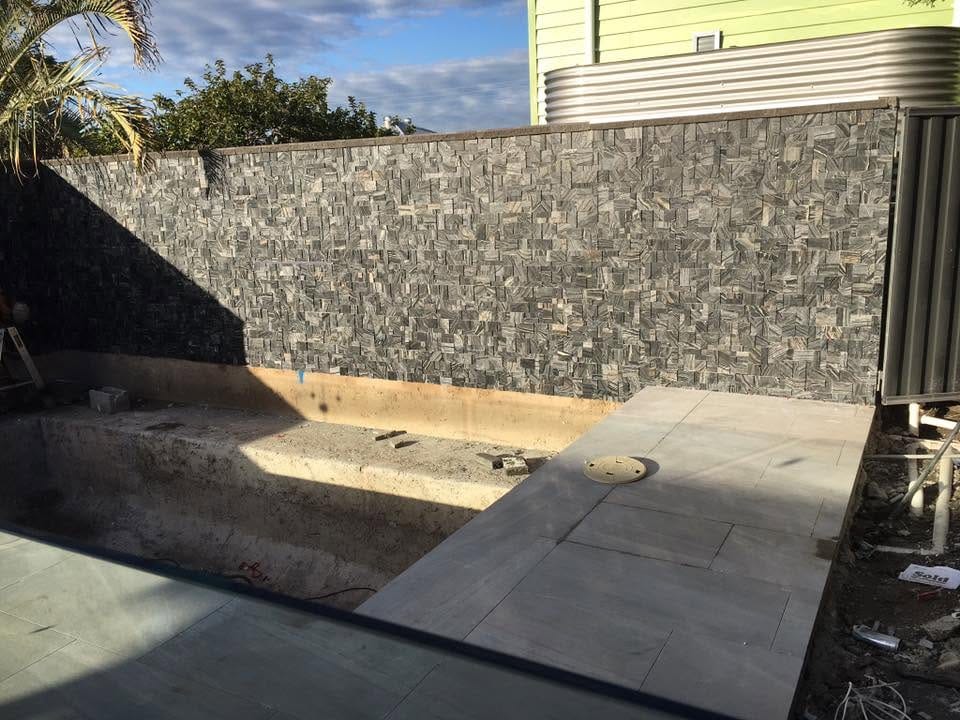 Pool surround with stone feature wall and glass fencing — pool surrounds and outdoor tiling in Brisbane by Torrisi Tiling